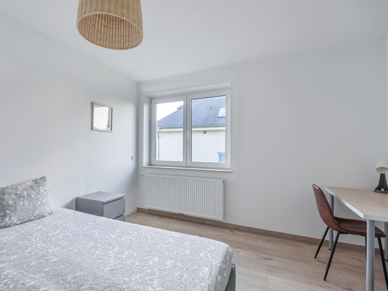 Furnished room for rent in coliving Luxembourg. It includes a double bed, bedside table, desk, chair, shelf, big wardrobe.