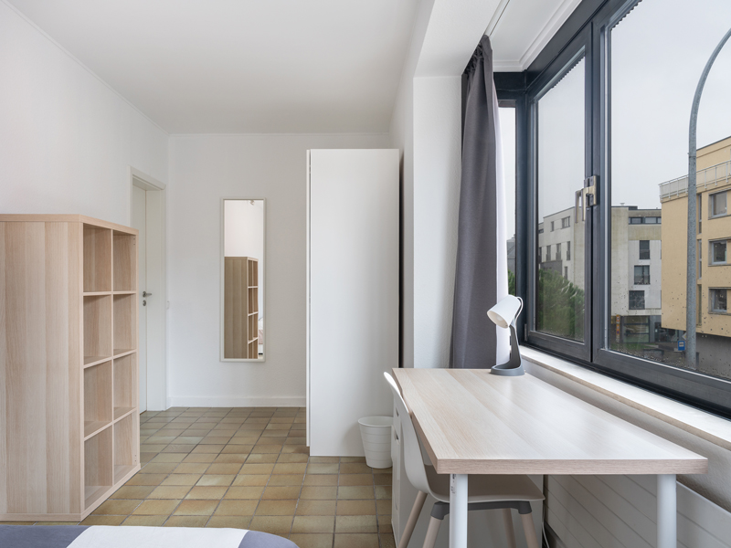 Furnished room for rent Luxembourg. It has a large window, double bed, bedside table, desk, chair, mirror, shelf, wardrobe