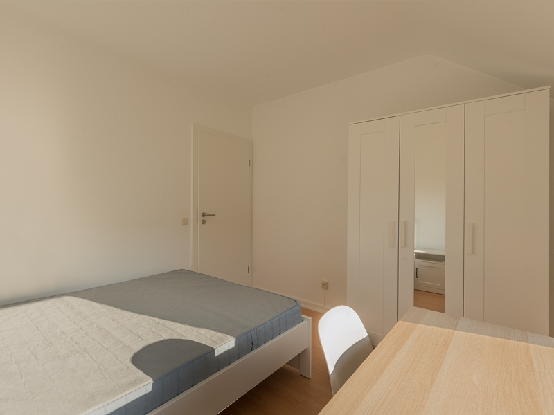 Furnished room in colocation Luxembourg, Belair. It includes a double bed, bedside table, desk, chair and wardrobe.
