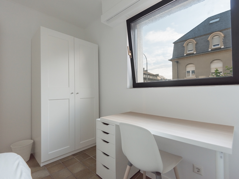 Furnished room for rent - Colocation Luxembourg. It includes a double bed, a wardrobe, a desk, and a chair.
