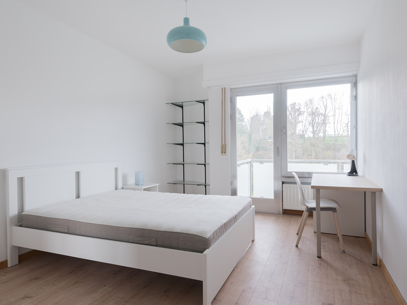 Furnished room for rent in Luxembourg City. The room includes a double bed, desk, chair, wardrobe and shelf.