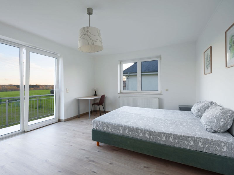 Furnished Room Luxembourg City. The room includes a double bed, bedside table, desk, chair, wardrobe, mirror and a shelf.