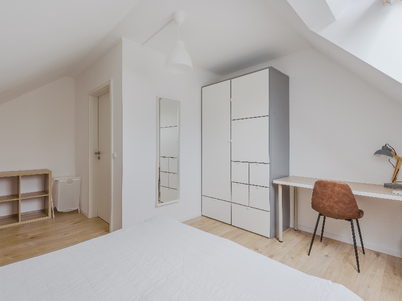 Furnished room for rent in Luxembourg. The room includes a double bed, bedside table, wardrobe, desk, mirror, shelf and a chair.