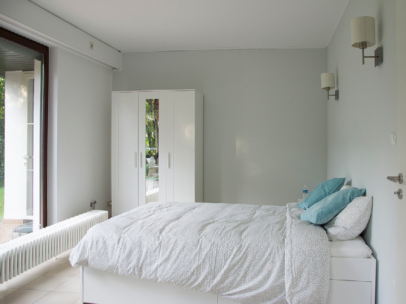 A brightly lit furnished bedroom in a Luxembourg houseshare, featuring a double bed and a wooden wardrobe.