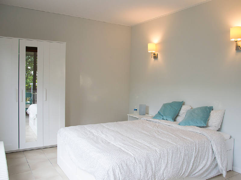 A brightly lit furnished bedroom in a Luxembourg houseshare, featuring a double bed and a wooden wardrobe.